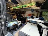 This RV rental interior features a Chicco car seat, portable fridge, Lagun table, and organized overhead storage with green LEDs.