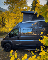Grey RV rental with pop-top tent immersed in vibrant golden aspen trees, reflecting mountains & sky, perfect for fall adventures.