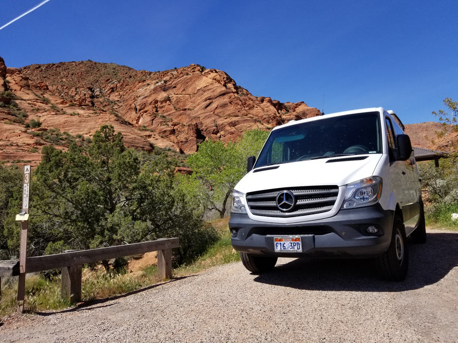 White Mercedes Sprinter rv rental parked by red rock mountains. Perfect for desert trips & scenic views.