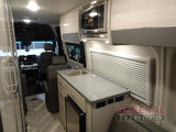 RV rental interior showing a compact kitchen with sink, microwave, and mini-fridge, with the driver's cabin visible.