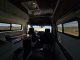 Spacious rv rental interior showing a driver on an open desert road, with custom cabinets and wooden ceiling.