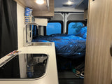 Step inside this cozy RV rental! Features a compact kitchen with sink, cooktop, and a starry bed for comfortable travel adventures.
