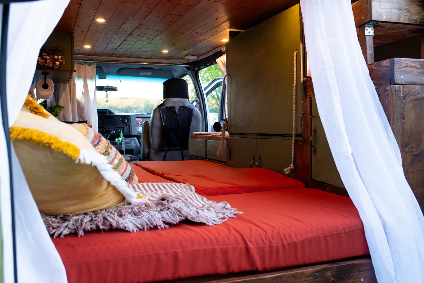 Inside this cozy RV rental: a custom van conversion features a comfy bed with orange cushions and wood accents.