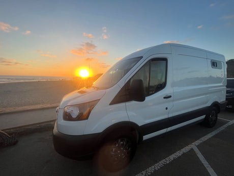 White RV rental van at a beach sunset. Enjoy beach camping and road trip adventures with this camper.