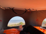 RV rental: Relaxing inside a pop-top camper, enjoying the serene oceanfront beach view. Ideal for cozy camping trips.