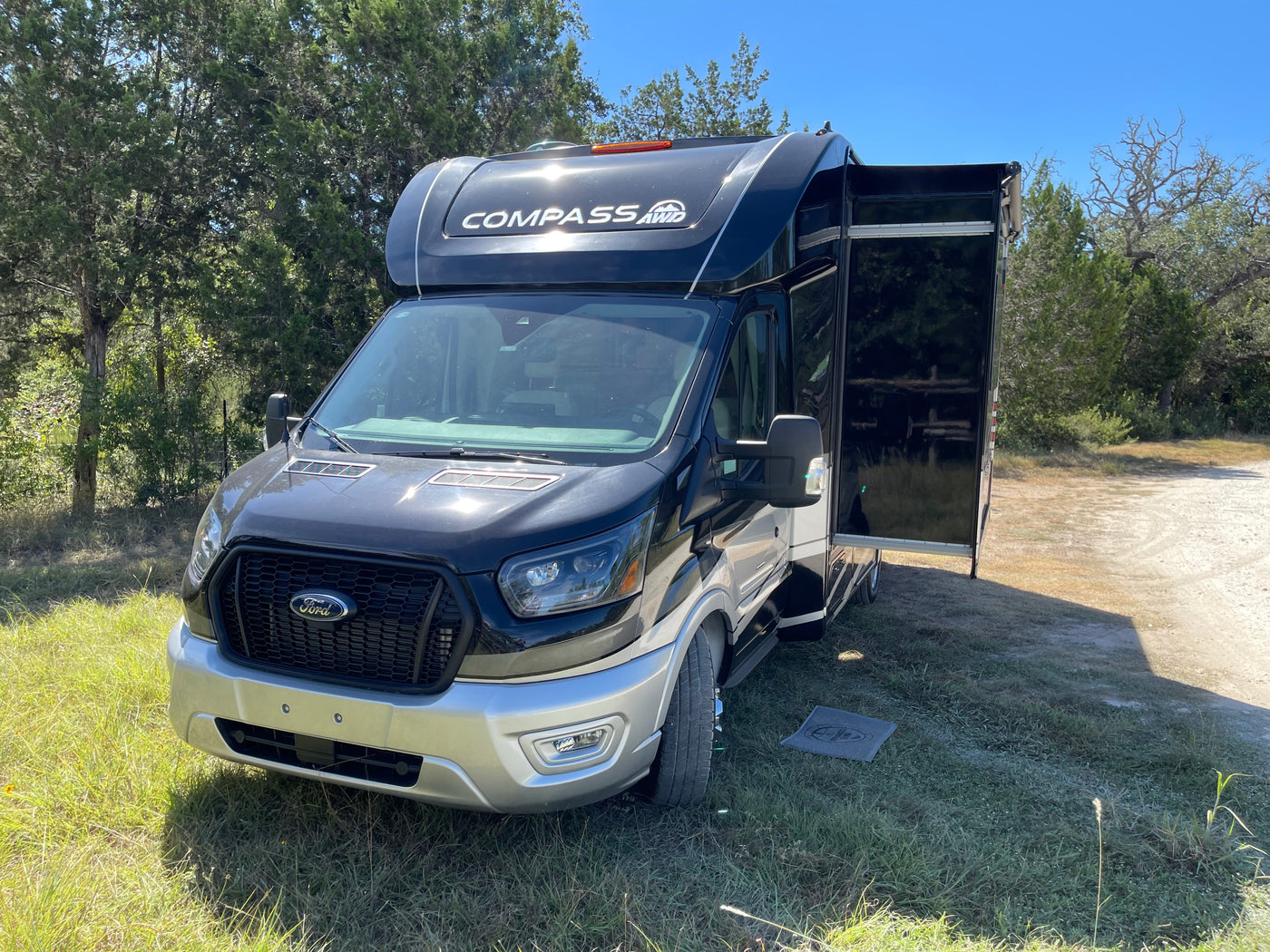 A black Ford Compass AWD RV rental (motorhome) with an open side door is parked on grass next to a dirt path. — photo 12
