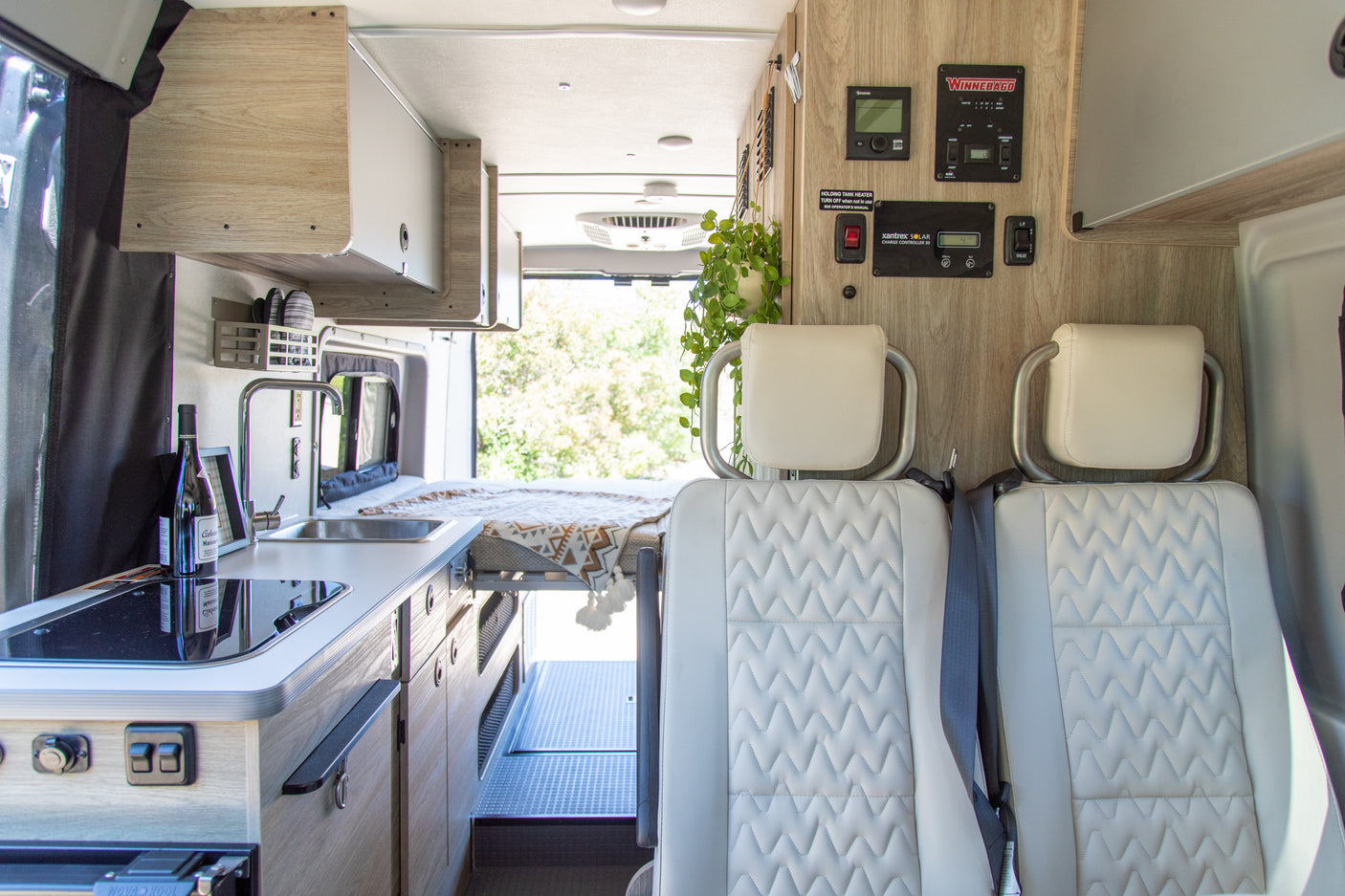 Bright rv rental interior: compact kitchen, comfortable rear bed, front seating, and essential control panels.