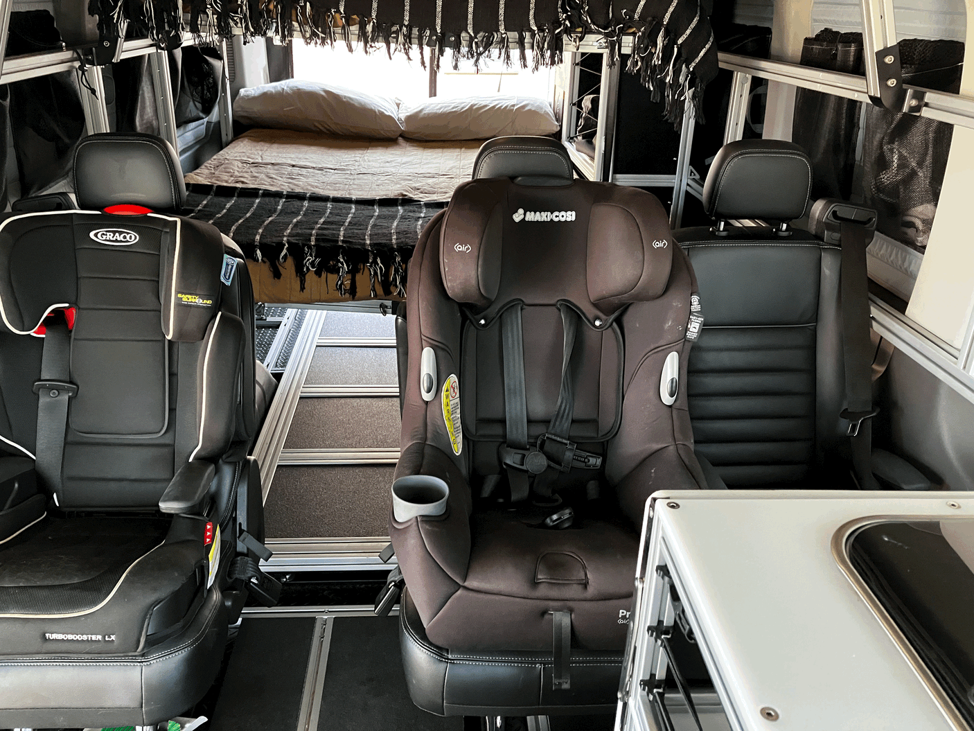 Modular RV rental interior featuring two child car seats & a bed for family adventures on the road.