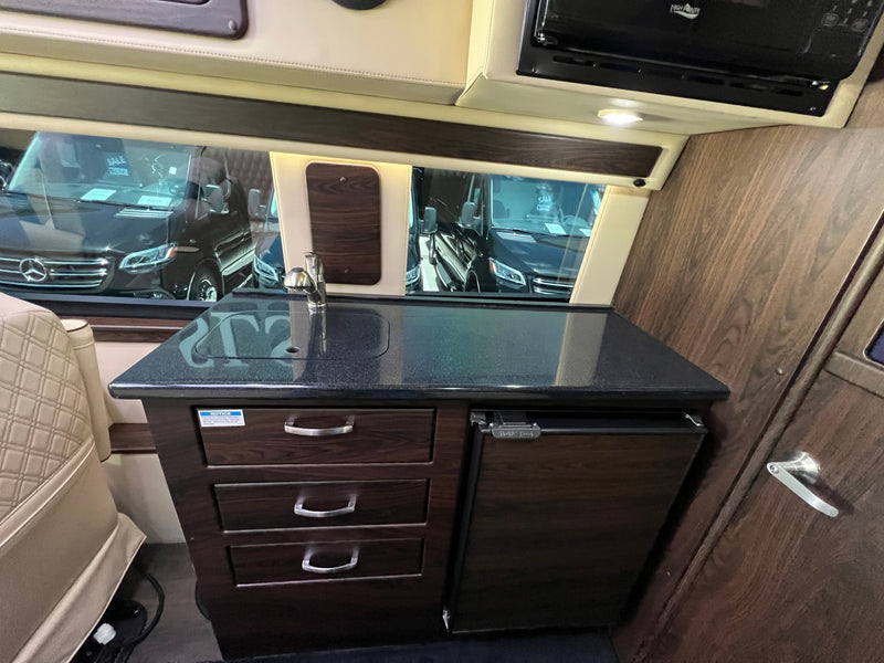 Compact RV rental kitchen area features a dark countertop, sink, faucet, microwave, and under-counter refrigerator. — photo 9
