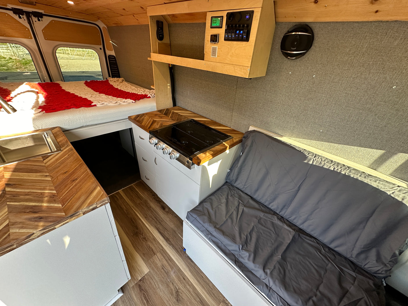 Interior of an RV rental showing a bed, kitchenette with wood counters and stove, plus bench seating. Perfect for travel.