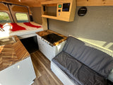 Interior of an RV rental showing a bed, kitchenette with wood counters and stove, plus bench seating. Perfect for travel.