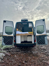 Open rear doors of a custom campervan reveal a cozy bed & storage. Perfect for RV rental adventures in frosty landscapes.