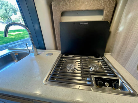 RV rental kitchen with stainless steel sink, gooseneck faucet, and Dometic two-burner stovetop with open cover.