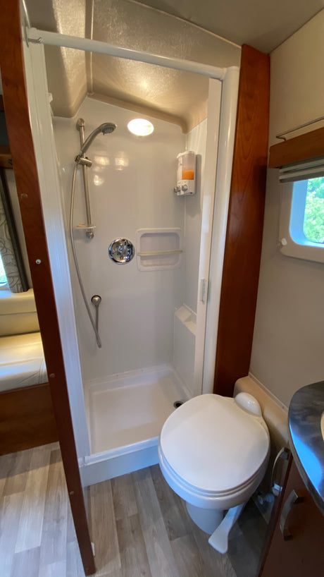 RV rental bathroom features a compact white shower stall with handheld shower, soap dispenser, and toilet.
