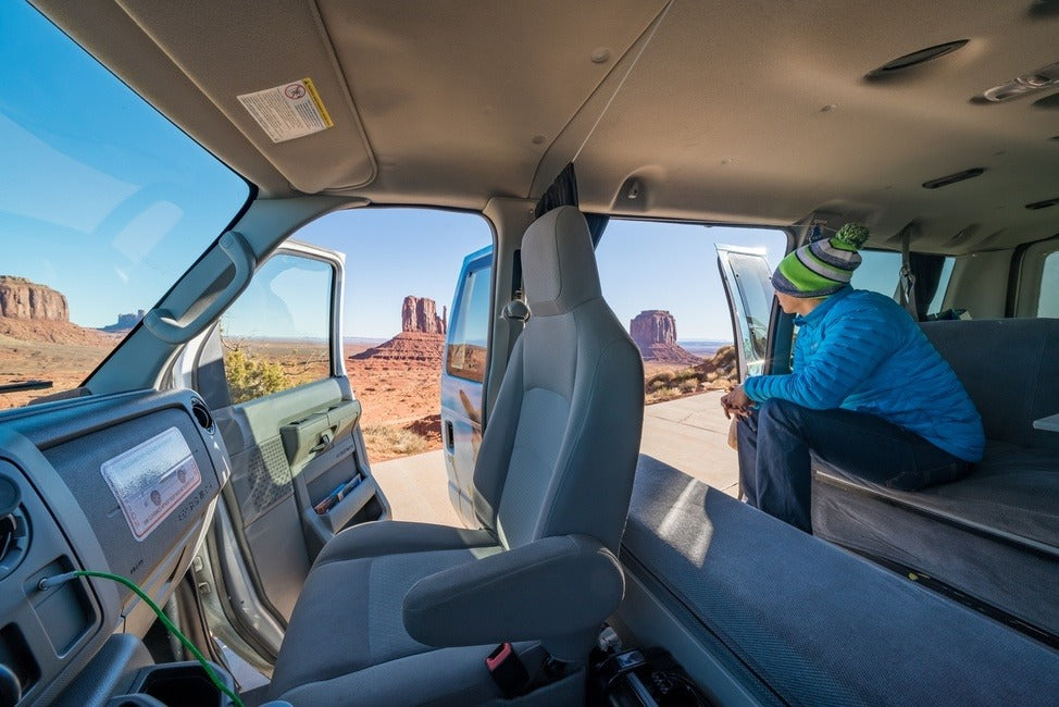 RV rental: Traveler enjoys stunning desert views from inside a parked camper van, ideal for road trips.