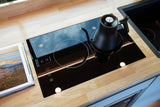 Compact RV rental kitchen features a sleek induction cooktop with a kettle on a light wood counter.