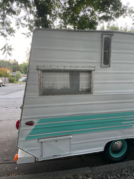 Vintage white RV rental with a distinctive teal stripe, parked on the street. Features a retro design and side windows.