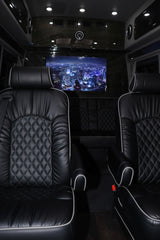 Luxury RV rental interior with plush black leather seats, diamond stitching, and an entertainment screen showing a cityscape.