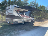 Enjoy the outdoors! This Thor Compass AWD RV rental is parked with its awning extended under a clear sky.