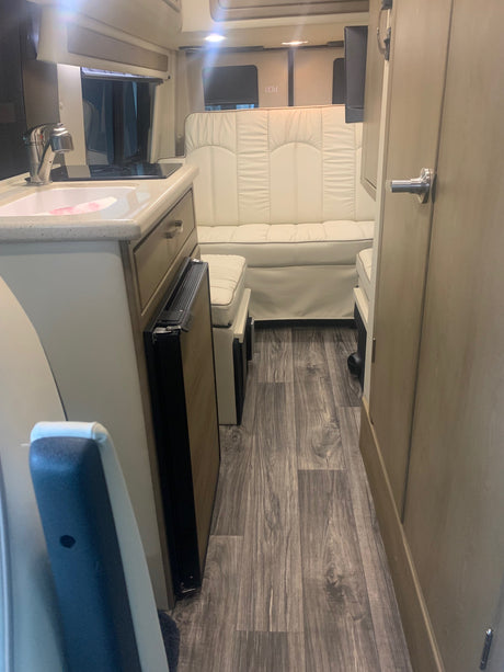 Modern rv rental interior with white seating, kitchen, and wood-style flooring.