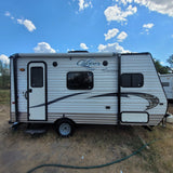 White and brown striped Clipper Coachmen travel trailer under a blue sky with clouds, perfect for an rv rental adventure.