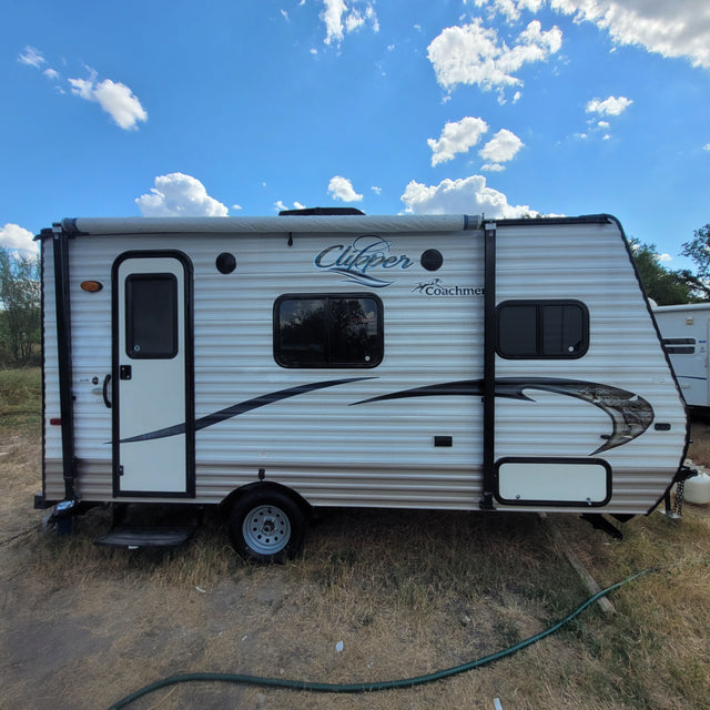 White and brown striped Clipper Coachmen travel trailer under a blue sky with clouds, perfect for an rv rental adventure.