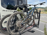 RV rental adventure: Two dusty mountain bikes are securely mounted on a hitch rack at the back of a white van.