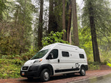 White rv rental campervan on a wet forest road, towering redwoods in the background. Adventure awaits!