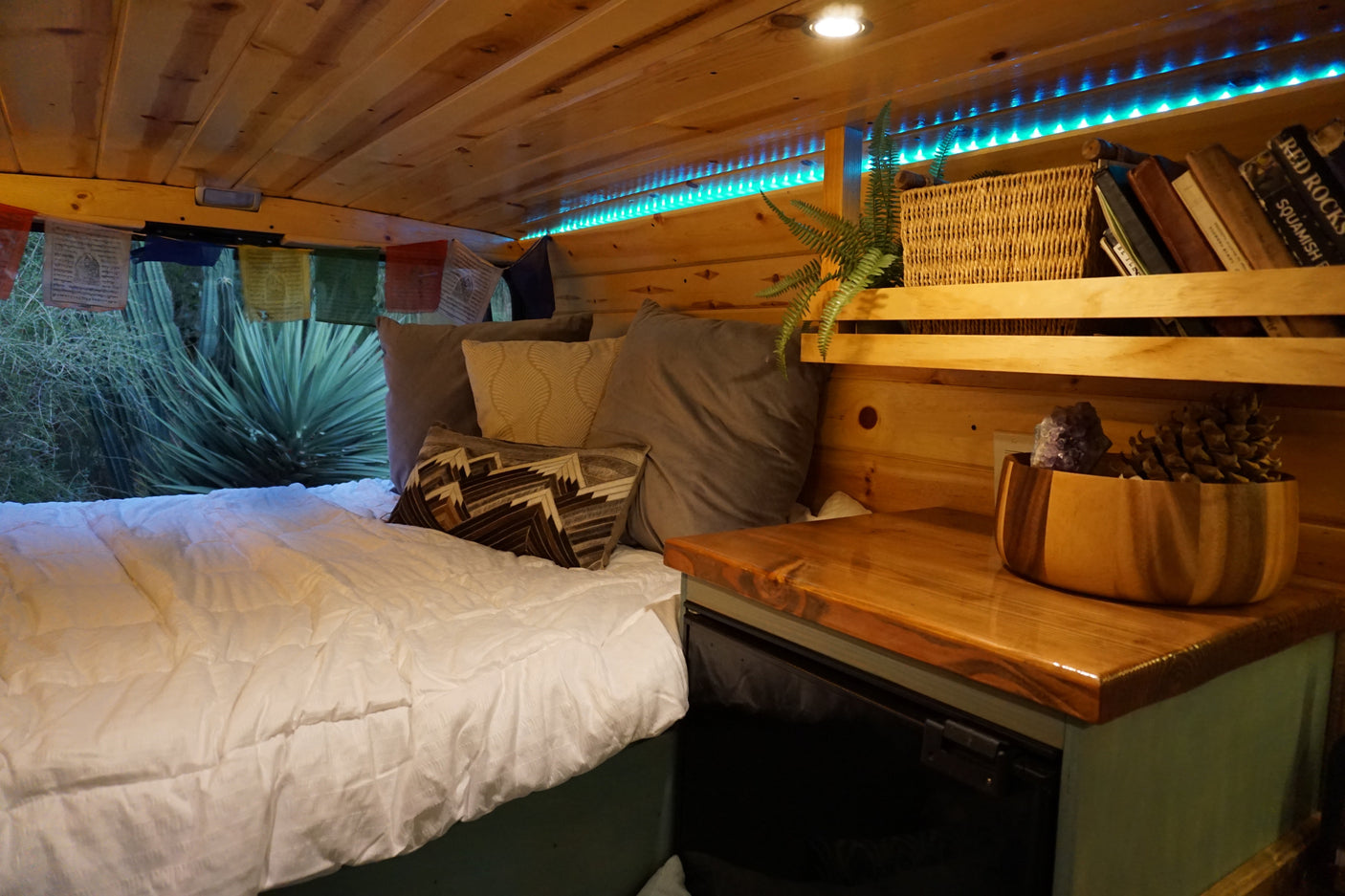 Cozy RV rental interior with wood paneling, comfortable bed, ambient blue lights, and clever storage solutions.