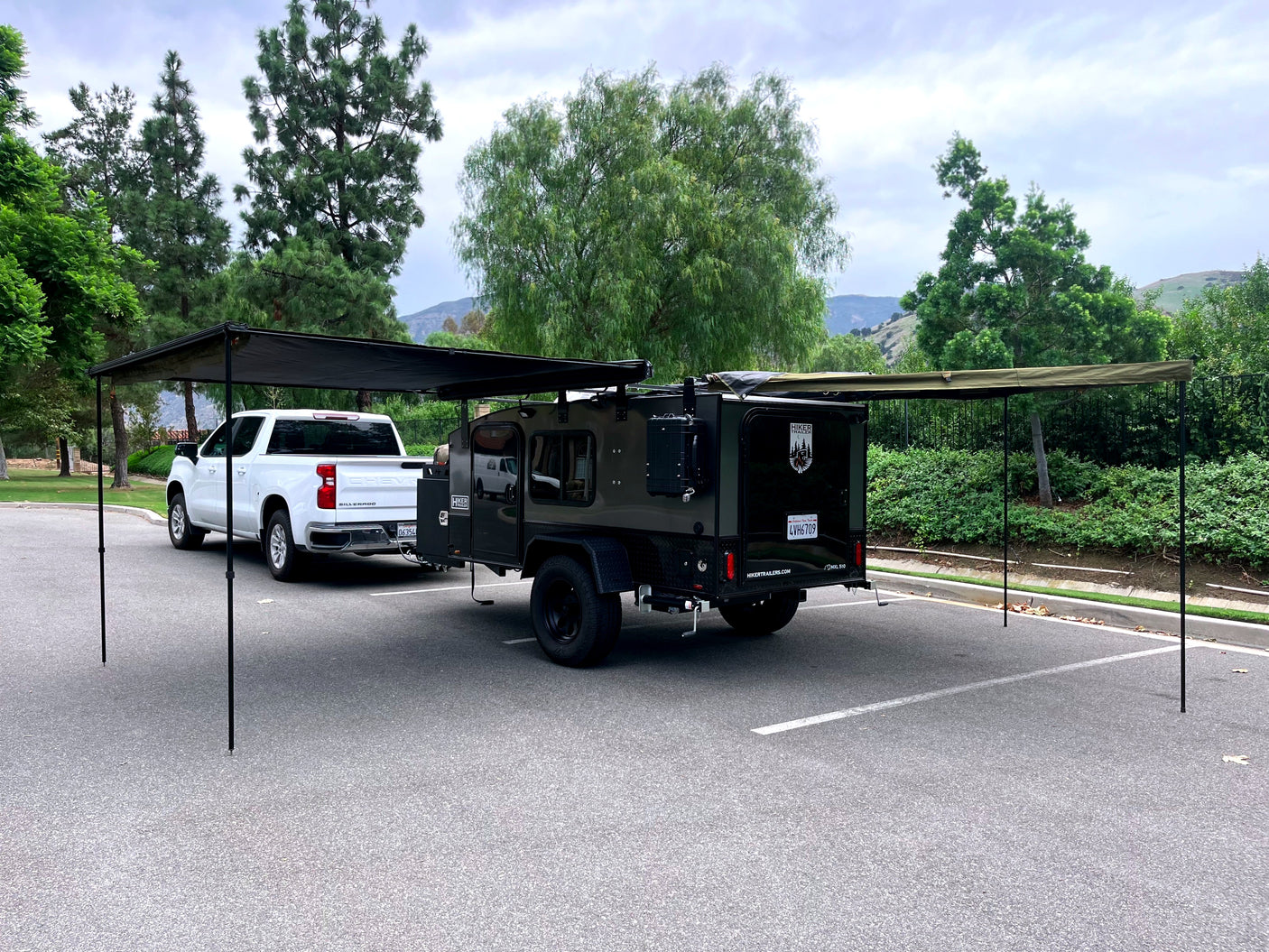 This rv rental setup showcases a white pickup truck towing a Hiker teardrop camper with extended awnings for shaded outdoor adventure.