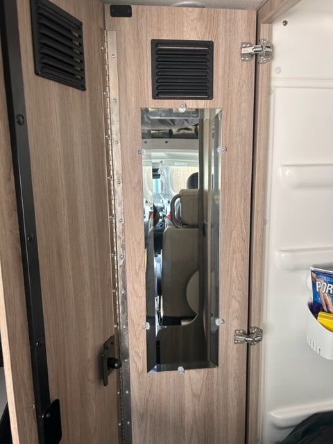 RV rental interior: Wood-paneled wall with a mirror, black vent, and storage hinges in a modern camper space.