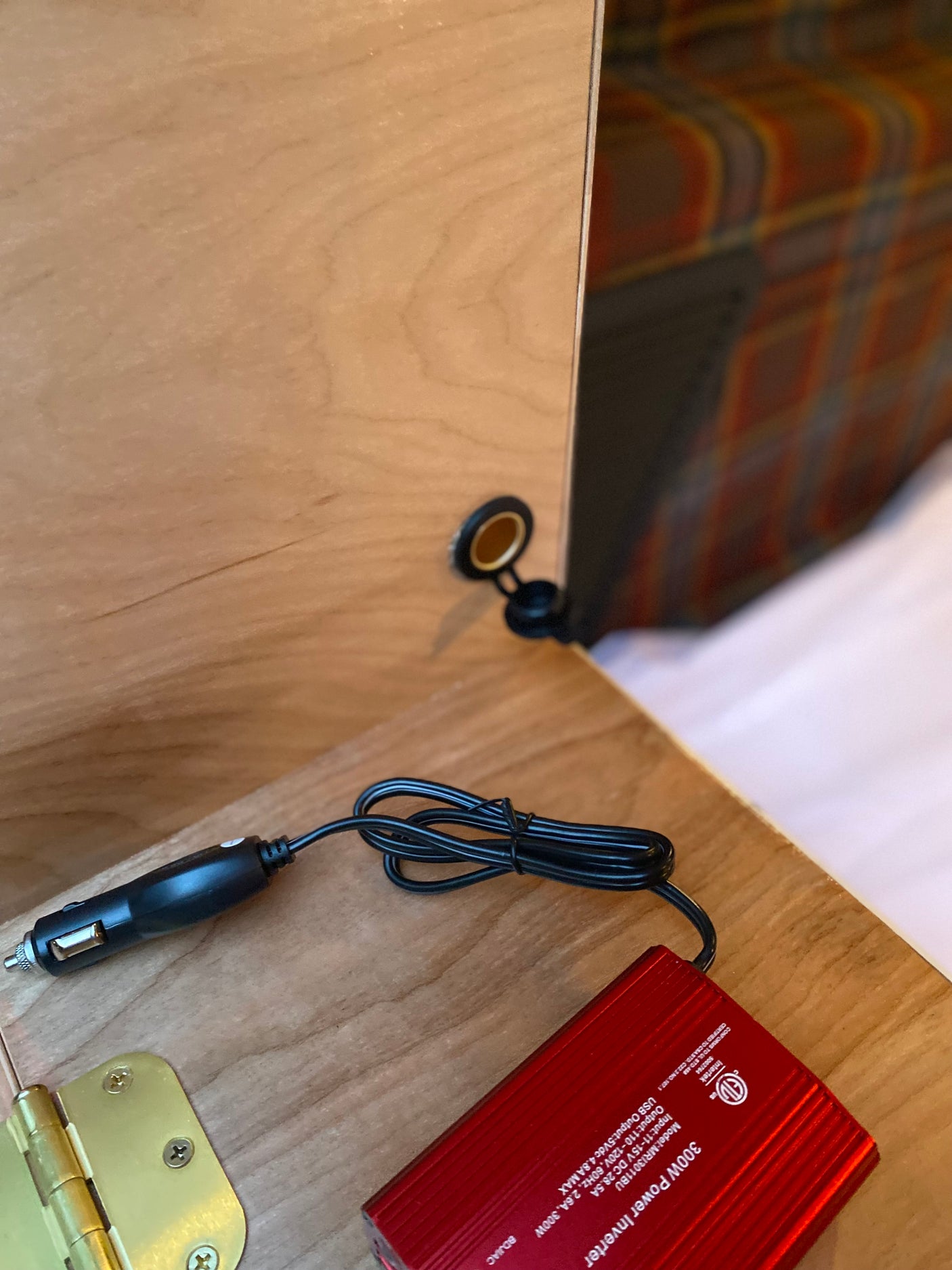 RV rental: Portable 300W power inverter with 12V plug & USB output connected to a wall socket in wood cabinetry.