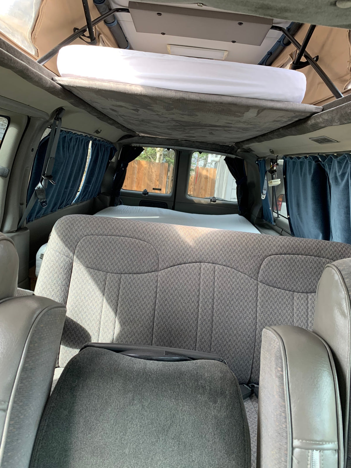 Inside an RV rental camper van: elevated pop-top bed, rear seats, and window curtains for a compact travel setup. — photo 8