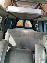 Inside an RV rental camper van: elevated pop-top bed, rear seats, and window curtains for a compact travel setup.