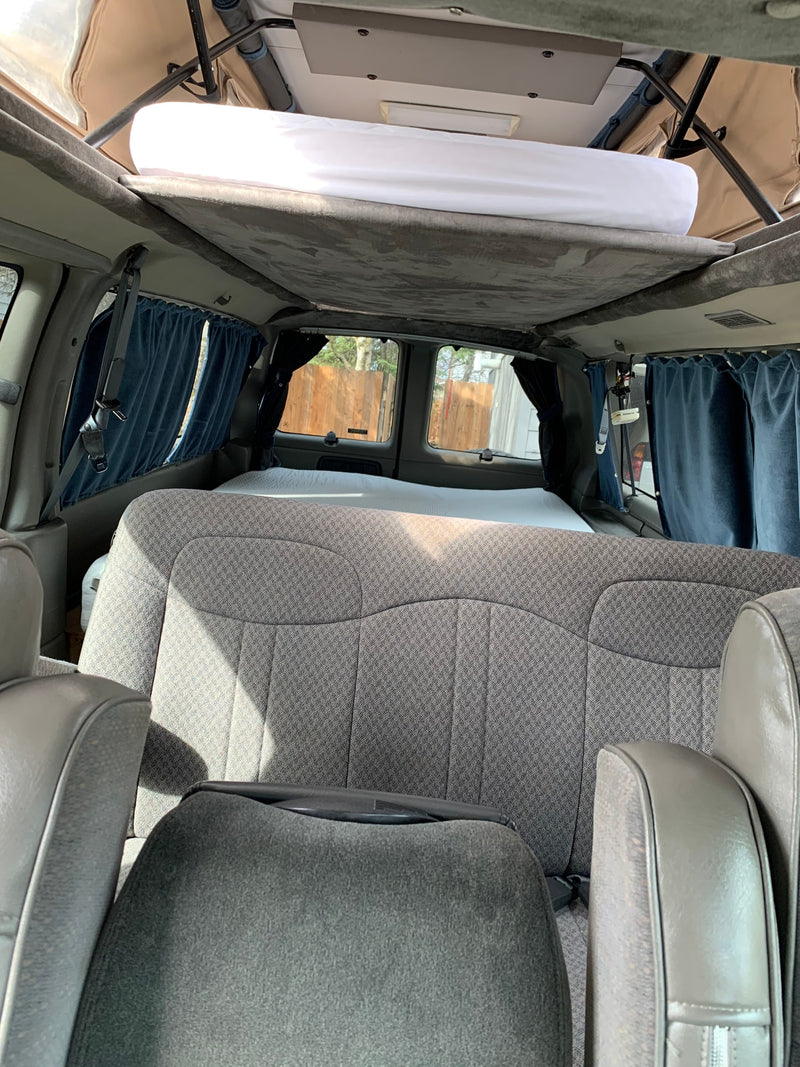 Inside an RV rental camper van: elevated pop-top bed, rear seats, and window curtains for a compact travel setup. — photo 8
