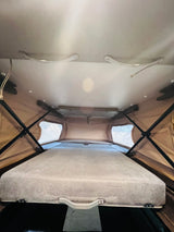 Inside an RV rental, this pop-up roof tent offers a cozy sleeping area with a bed and structural support.