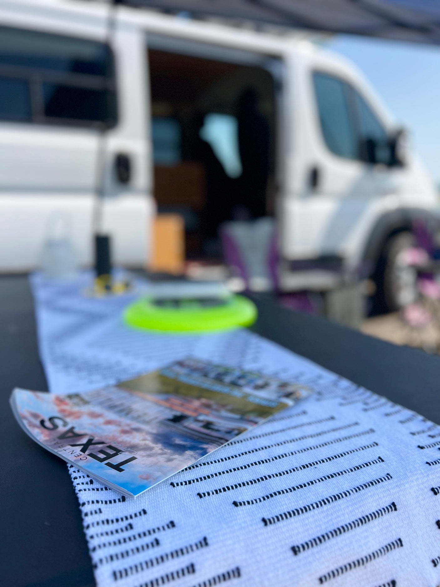 Explore Texas with an rv rental! Magazine on outdoor table in front of a white camper van, perfect for road trips.