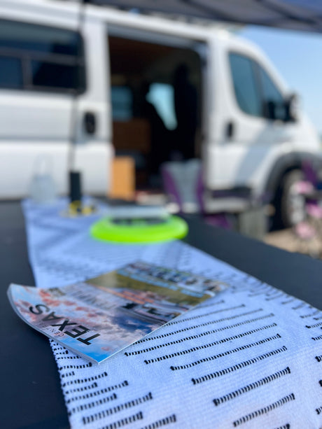 Explore Texas with an rv rental! Magazine on outdoor table in front of a white camper van, perfect for road trips.