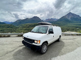 A white camper van, ideal for RV rental, parked in a stunning mountain landscape under cloudy skies, ready for adventure.