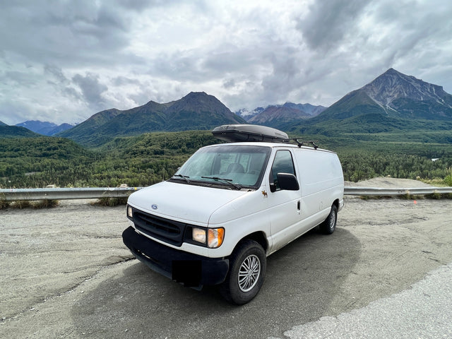 A white camper van, ideal for RV rental, parked in a stunning mountain landscape under cloudy skies, ready for adventure.