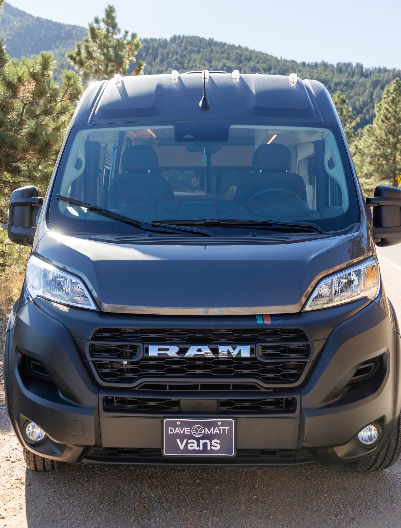 Front view of a dark gray Ram ProMaster campervan, likely an RV rental, parked on a dirt road in the mountains. — photo 7