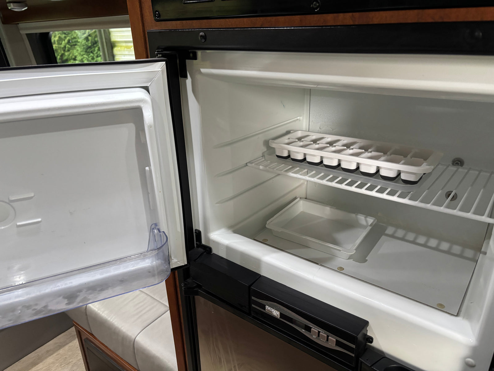 Inside an open Norcold RV refrigerator, showing clean shelves, ice cube trays, and a plastic bin. Ideal for your rv rental.
