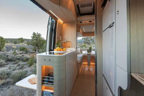 Modern RV rental living space: a stylish van conversion with kitchen, dining area, and panoramic outdoor views.