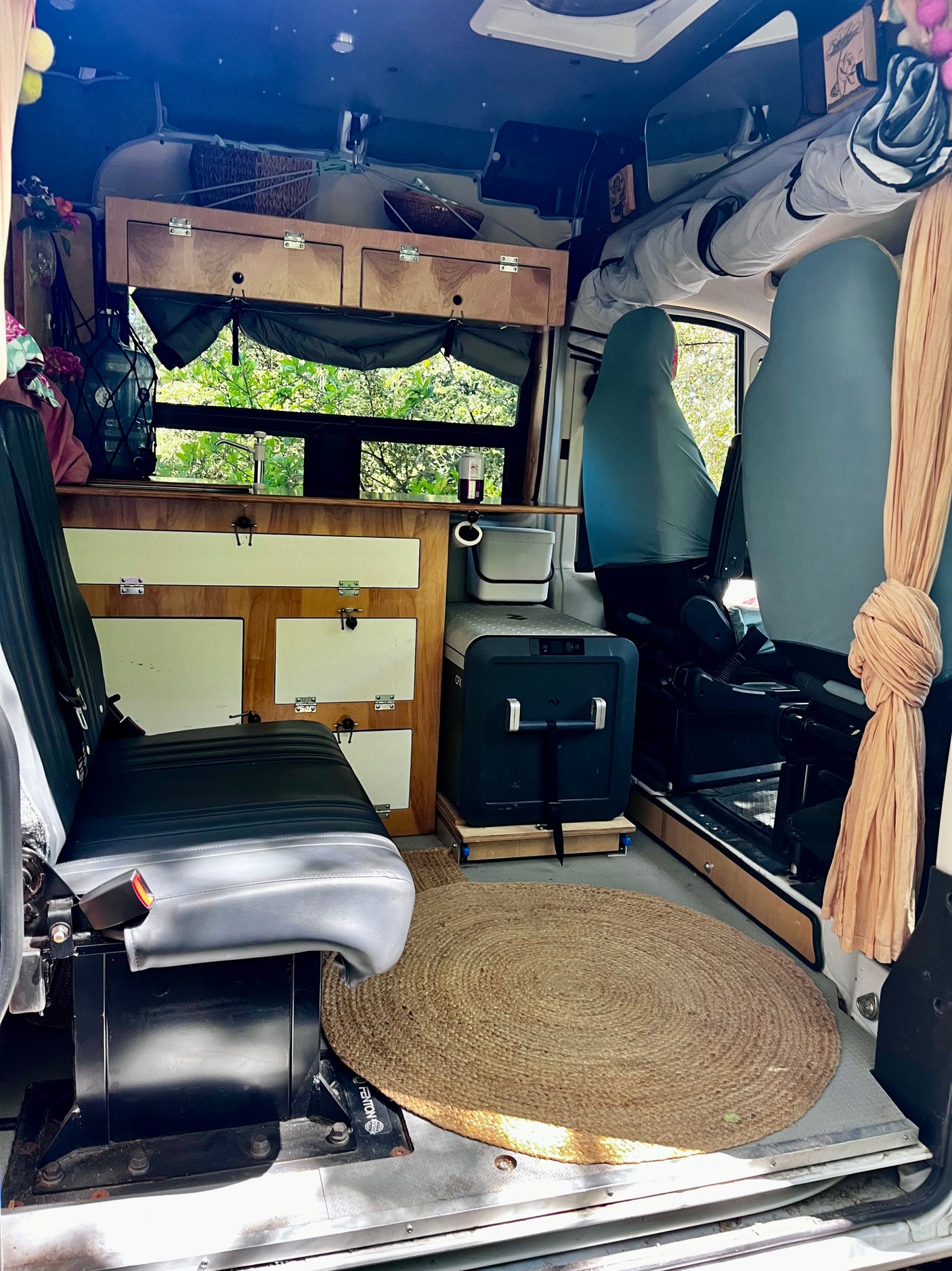 RV rental: Step inside this cozy camper van, featuring custom wood cabinets, comfortable seating, a portable fridge, and a round rug.