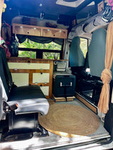 RV rental: Step inside this cozy camper van, featuring custom wood cabinets, comfortable seating, a portable fridge, and a round rug.