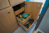 Organized RV rental kitchen storage with bamboo pull-out drawers holding dishes, pots, and mugs.