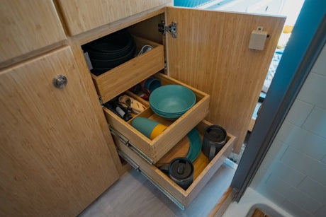 Organized RV rental kitchen storage with bamboo pull-out drawers holding dishes, pots, and mugs.