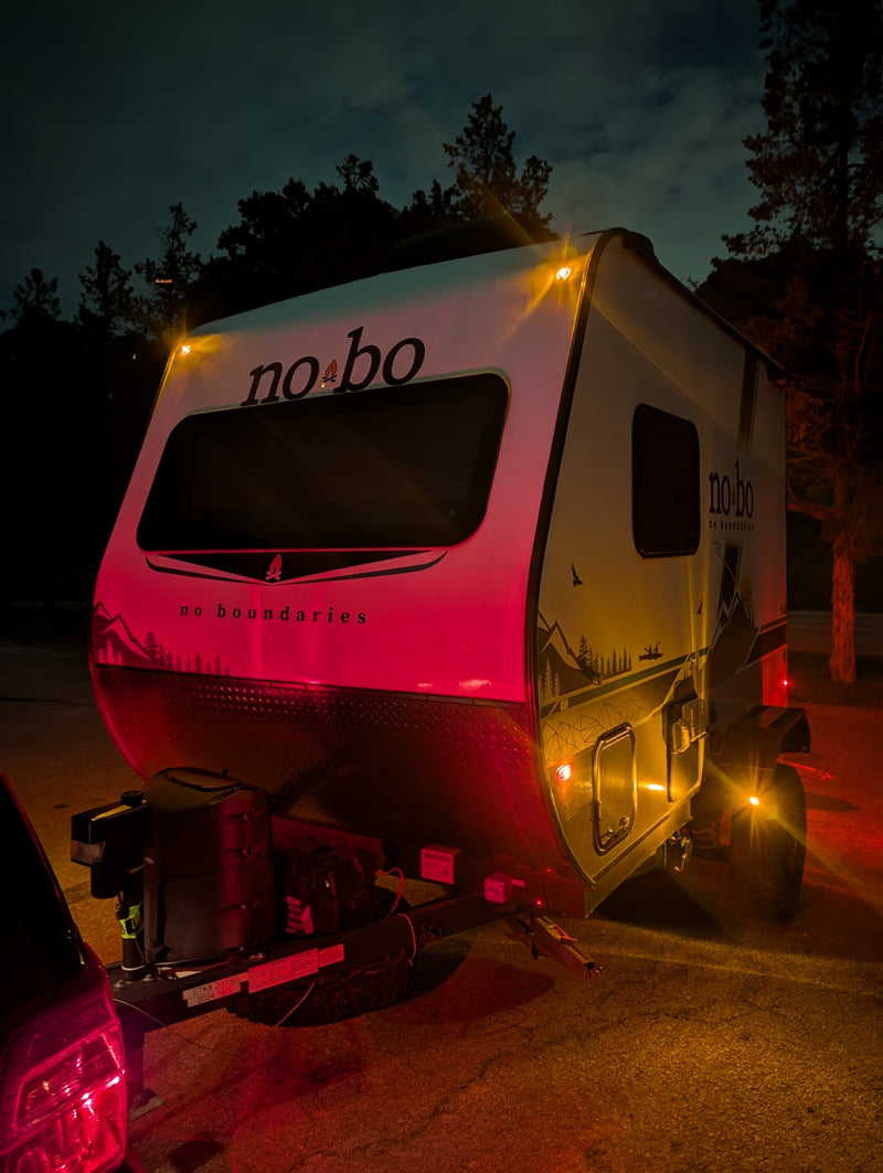 Nighttime rv rental featuring a No Boundaries travel trailer hitched to a car, illuminated by vibrant red and amber lights. — photo 3