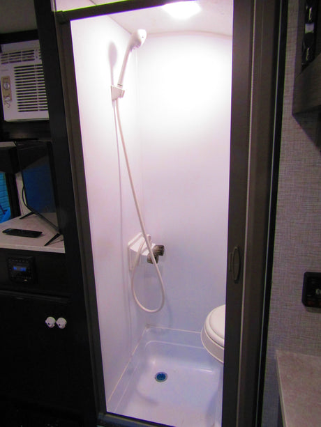 RV rental: View of a compact wet bath featuring a shower, toilet, and nearby air conditioner and entertainment unit.