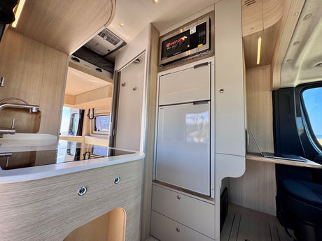 Modern RV rental interior: kitchenette with fridge/microwave, sleek design, and compact workspace for mobile living.